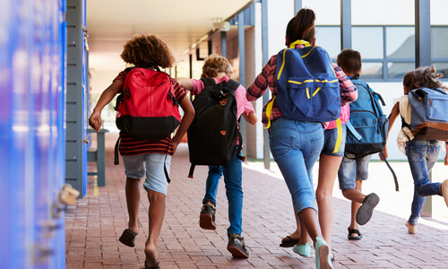 Kids running on school sidewalk with their backpacks on