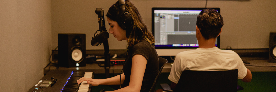 Two people working at recording studio with headphones, microphones, keyboard, and computer