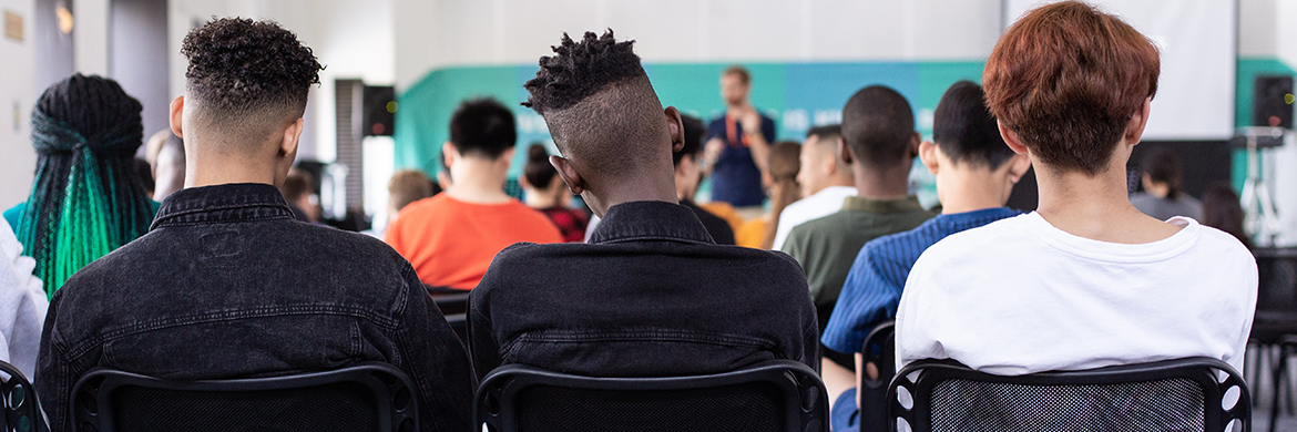 the back view of three teen boys sitting next to each other during a school assembly